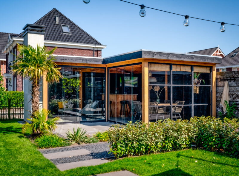 Tuinkamer op maat 7 Hoek vormige tuinkamer op maat met glazen schuifwand en buitenkachel